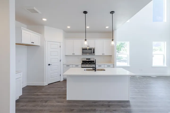 Modern kitchen featuring white cabinetry, a central island with a sink, stainless steel appliances, and wood-finish flooring