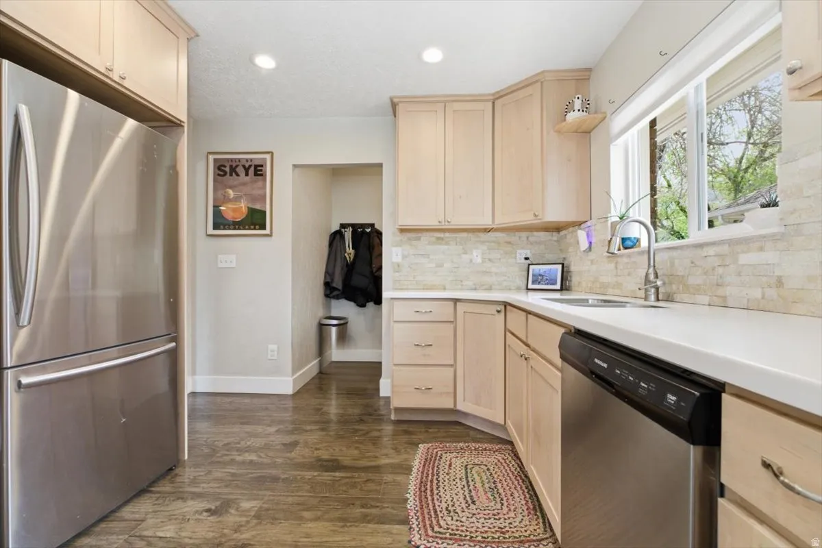 Kitchen featuring light wood finish cabinetry, stainless steel appliances, dark wood finished floors, recessed lighting, and backsplash