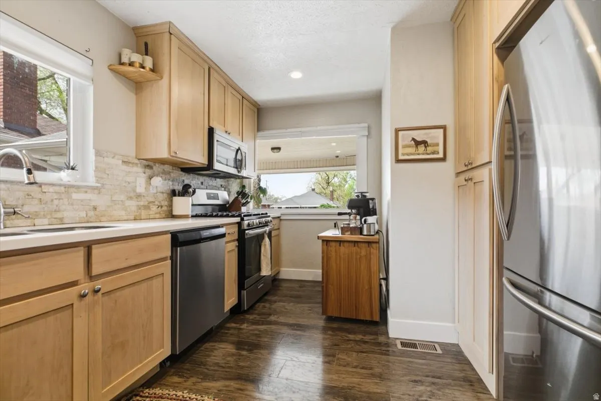 Kitchen featuring light wood finish cabinetry, stainless steel appliances, light countertops, dark wood-style floors, and recessed lighting