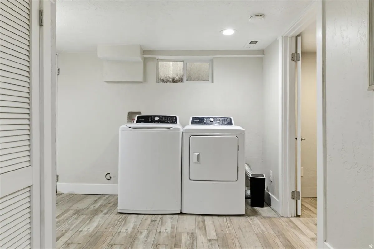 Laundry area featuring light wood-type flooring, washer and dryer, and recessed lighting