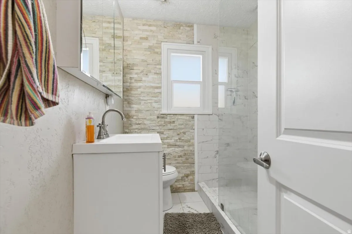 Bathroom 1 with vanity, a walk in shower stall, and tiled feature wall