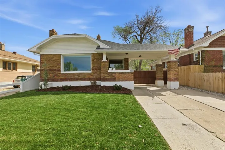 View of front of home featuring brick siding, concrete driveway, and a carport, and an automatic gate