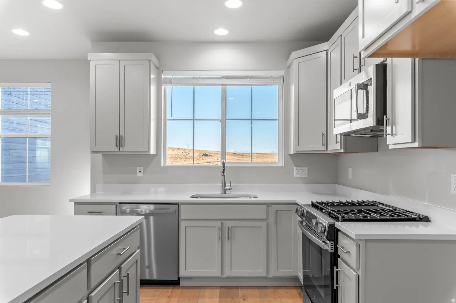 Kitchen featuring stainless steel appliances, healthy amount of natural light, recessed lighting, light wood-type flooring, and light stone counters