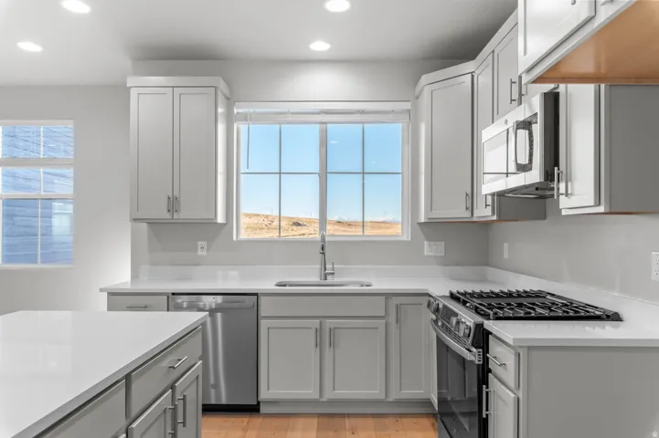 Kitchen featuring stainless steel appliances, healthy amount of natural light, recessed lighting, light wood-type flooring, and light stone counters