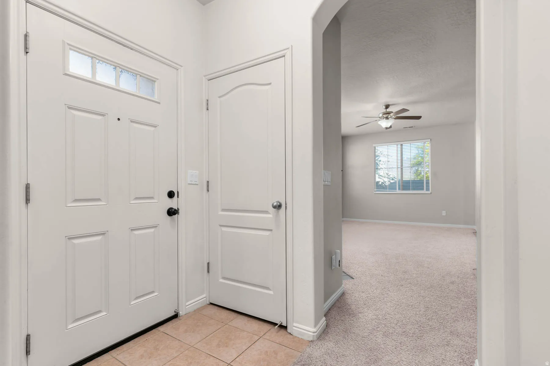Entrance foyer with light carpet, light tile patterned flooring, ceiling fan, and arched walkways