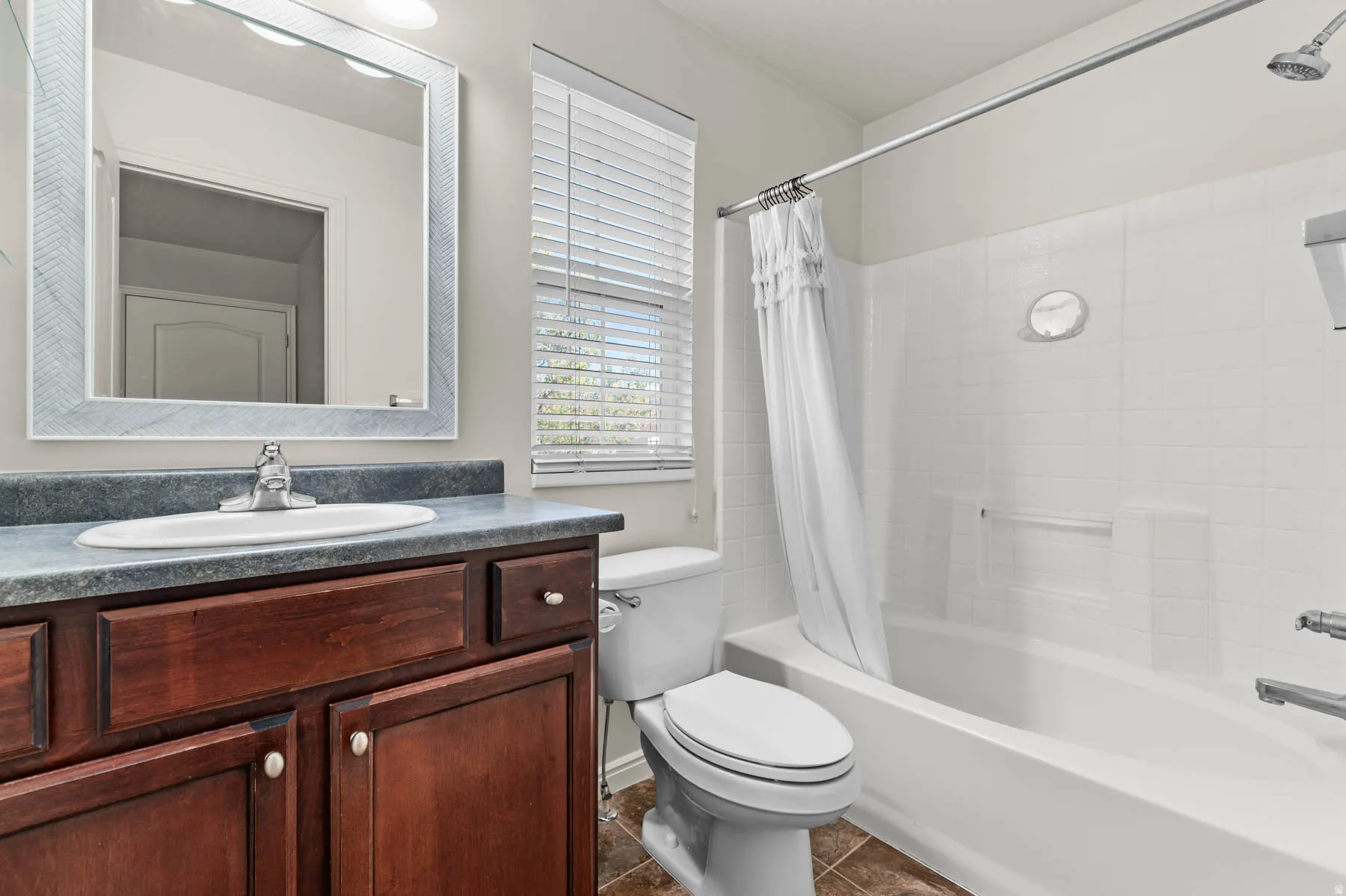 Bathroom with vanity, shower / bathtub combination with curtain, and dark tile patterned flooring