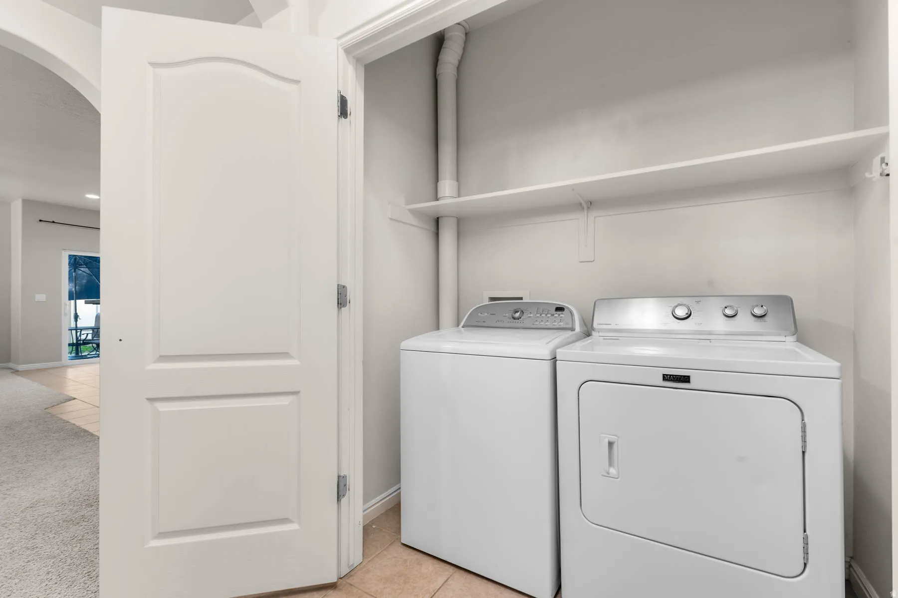 Laundry area with light tile patterned floors, arched walkways, light colored carpet, and washer and clothes dryer