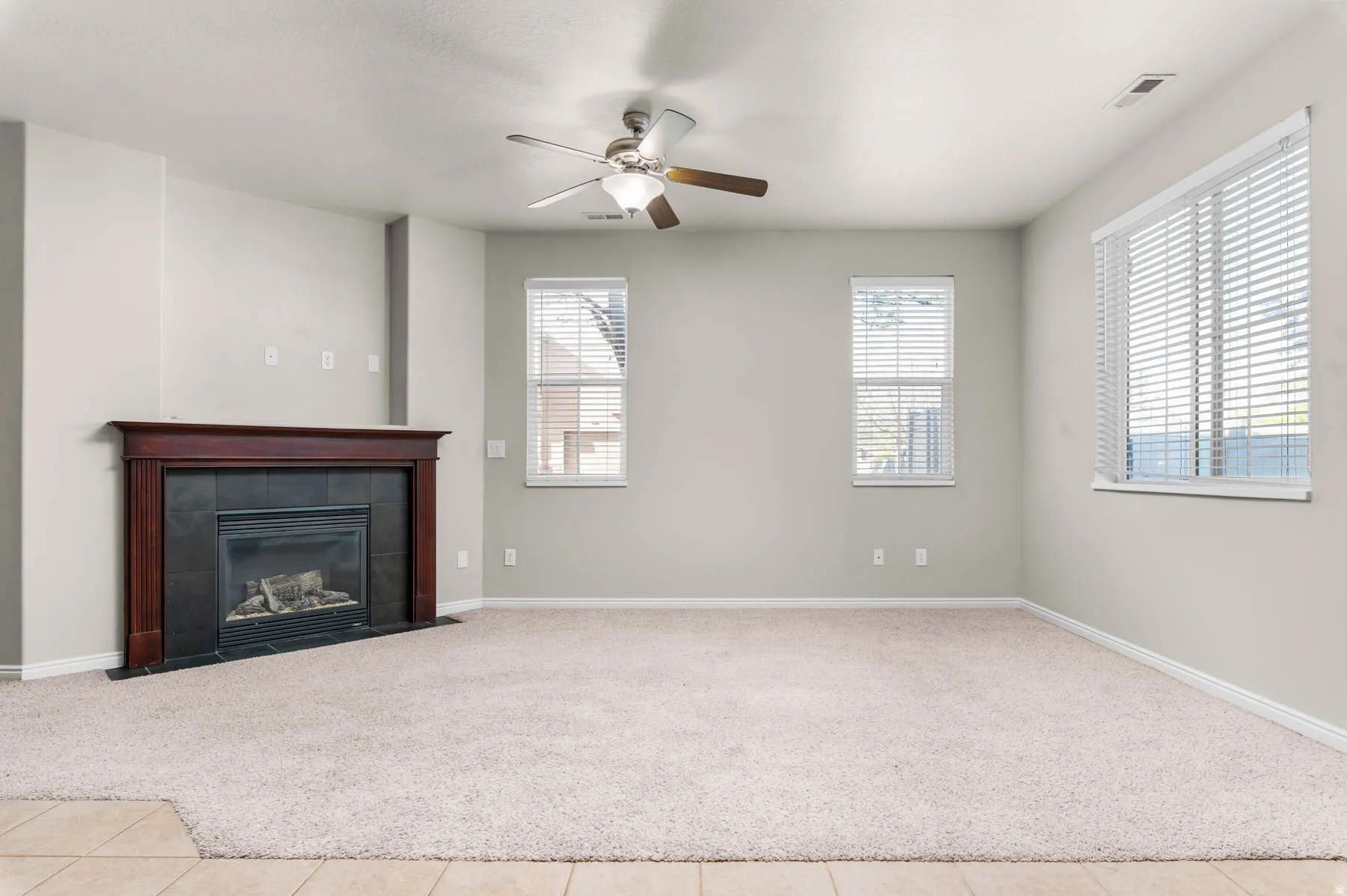Unfurnished living room with ceiling fan, a tile fireplace, carpet, and tile patterned flooring