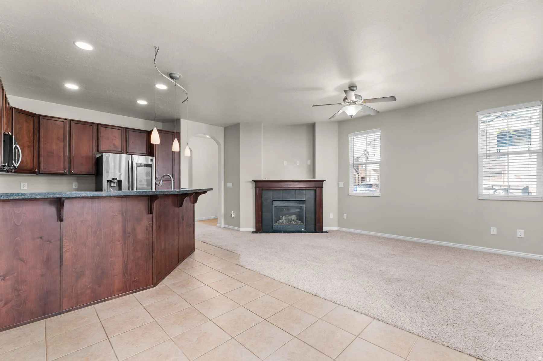 Kitchen featuring arched walkways, a breakfast bar, light colored carpet, light tile patterned flooring, and stainless steel appliances