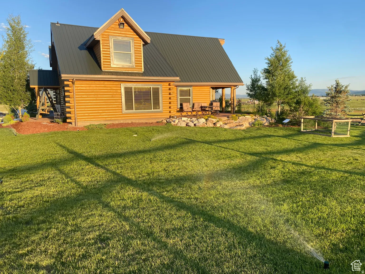 Back of property featuring log siding, a metal roof, a patio area, and a lawn