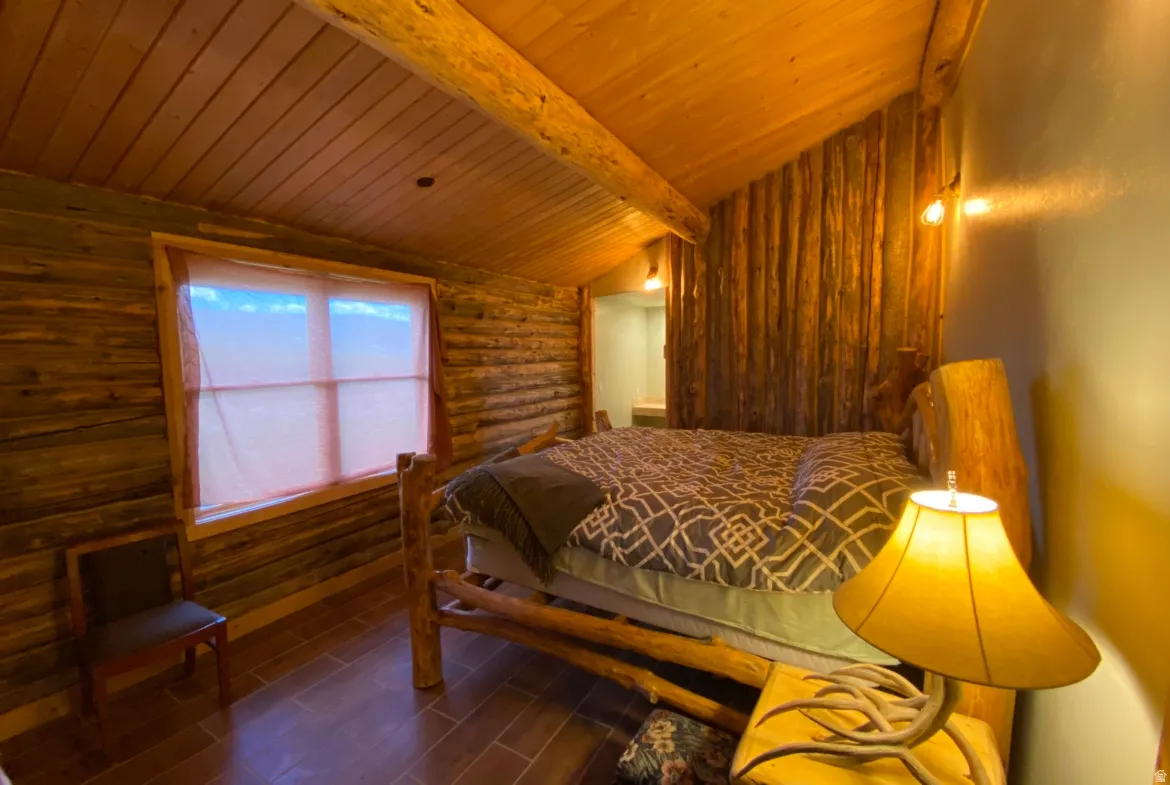 Bedroom featuring log walls, wooden ceiling, dark wood-style flooring, and vaulted ceiling with beams
