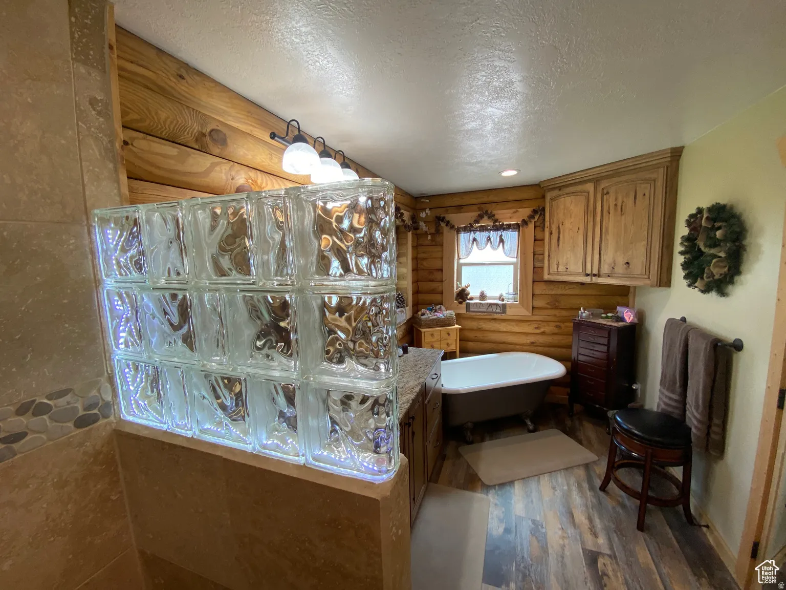Bathroom featuring log walls, a textured ceiling, a freestanding bath, dark wood-style flooring, and vanity