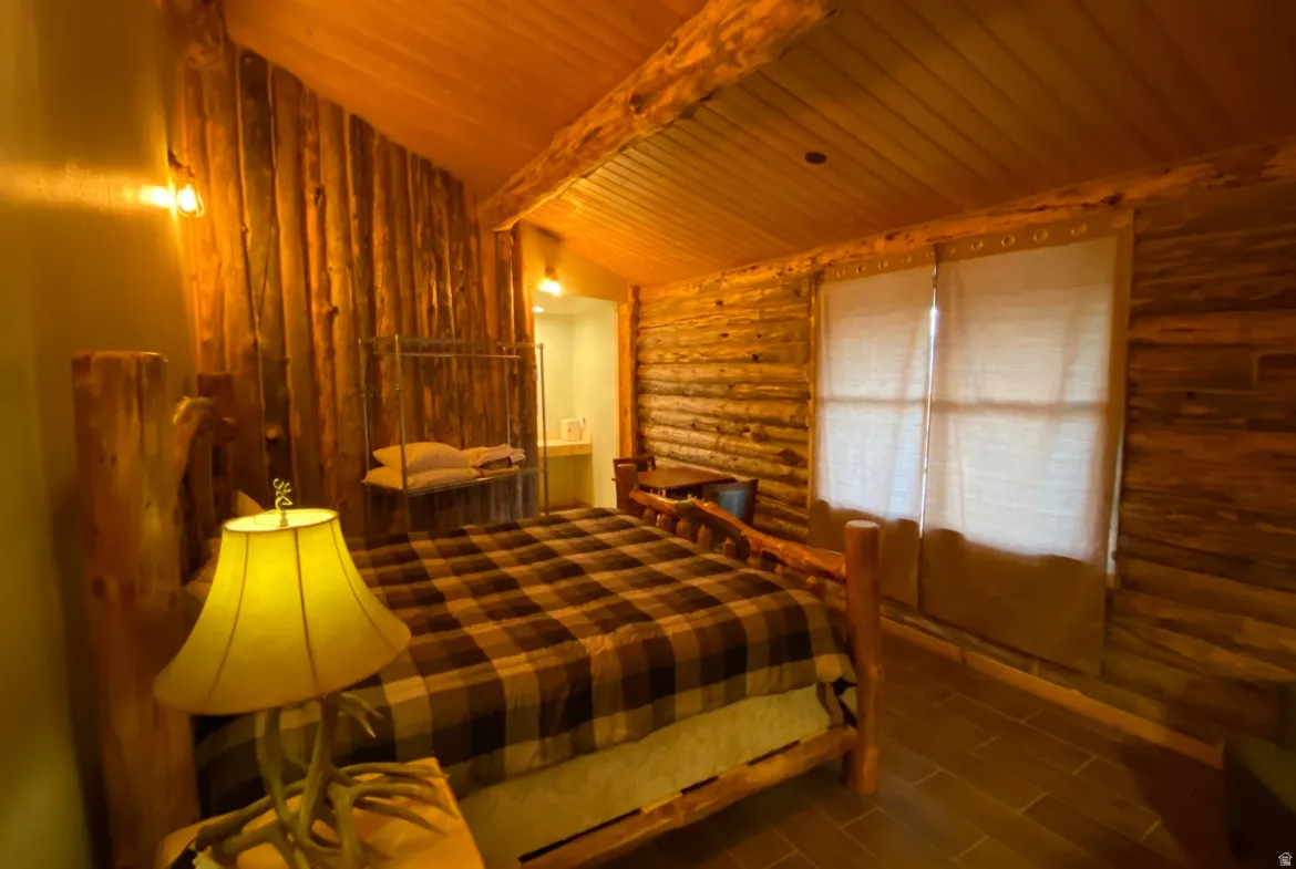 Bedroom featuring wooden ceiling, lofted ceiling with beams, wood tiled floors, and rustic walls