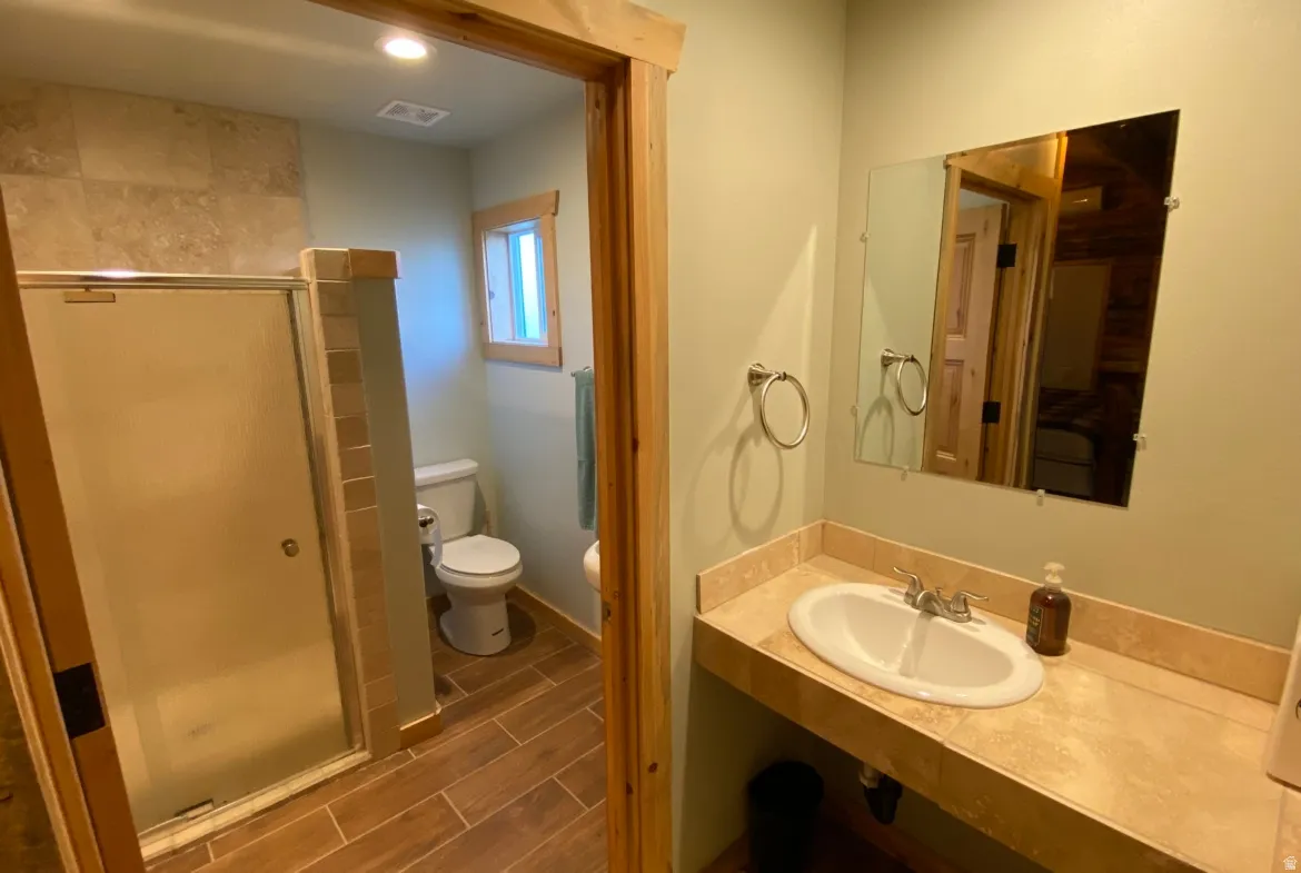 Bathroom featuring a shower stall, wood finish floors, vanity, and recessed lighting