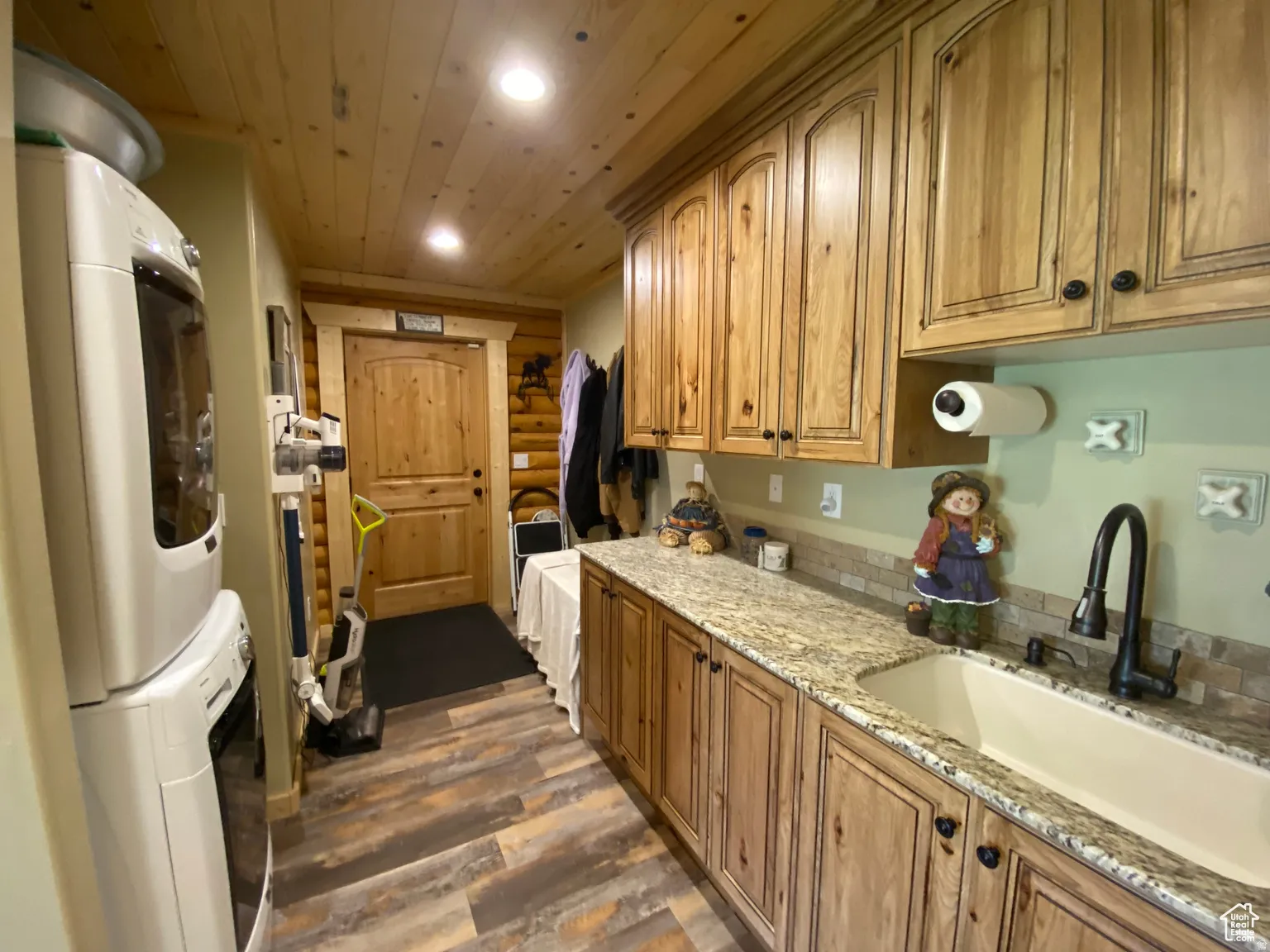 Kitchen with dark wood-style floors, recessed lighting, light stone countertops, stacked washer / dryer, and log walls