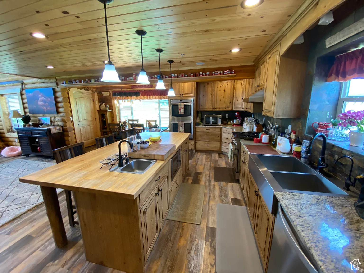 Kitchen featuring a center island with sink, log walls, a breakfast bar, wooden ceiling, and stainless steel appliances