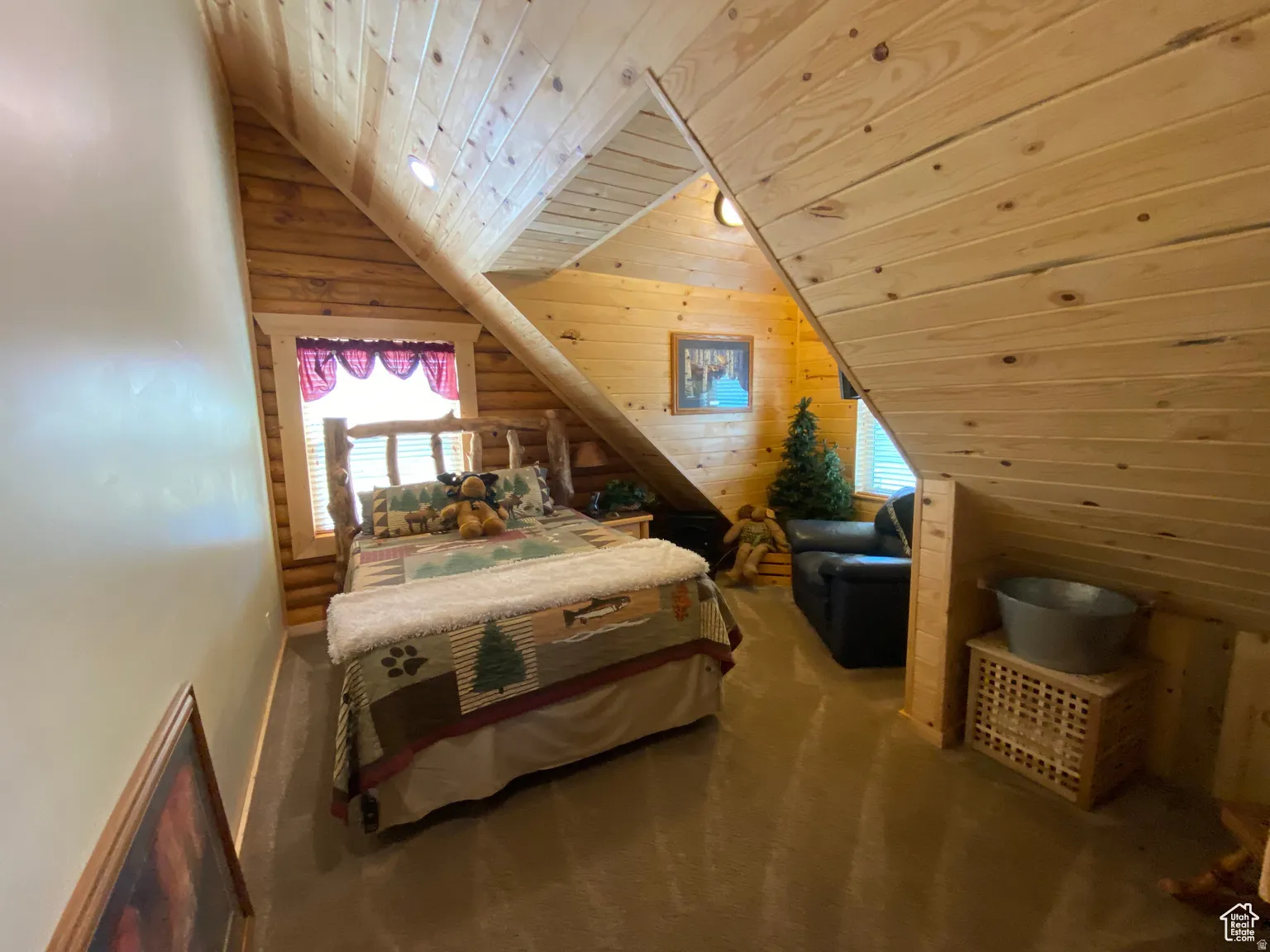Carpeted bedroom featuring a vaulted wooden ceiling, multiple windows, wooden walls, and log walls