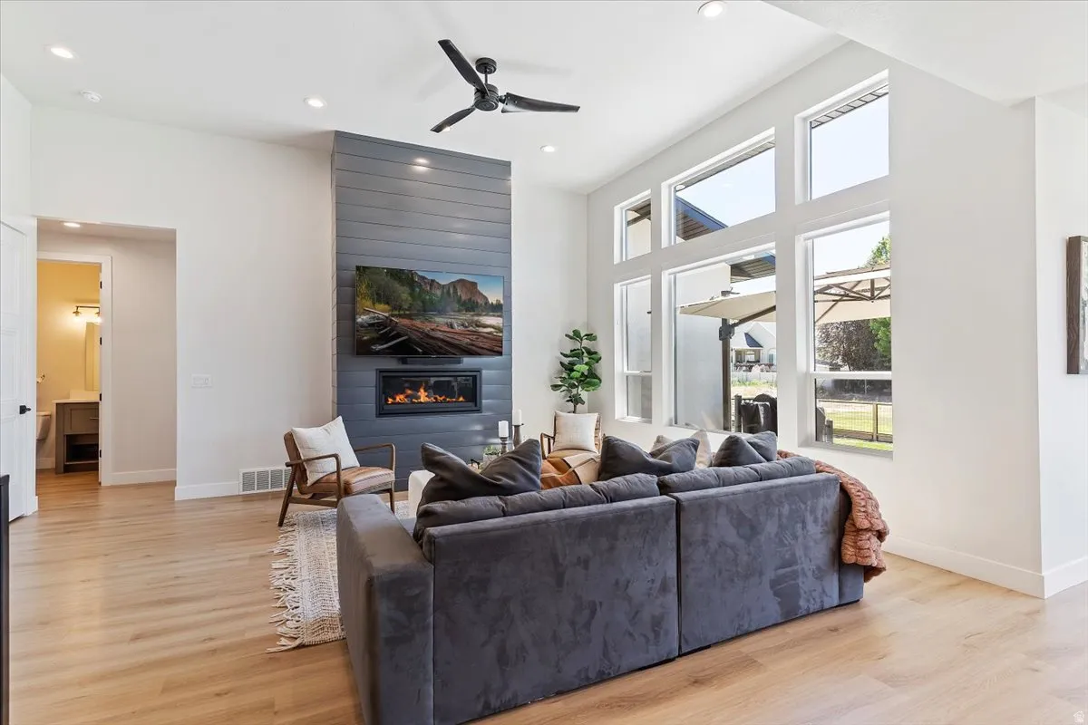 Living area featuring ceiling fan, light wood-style flooring, recessed lighting, a fireplace, and a high ceiling