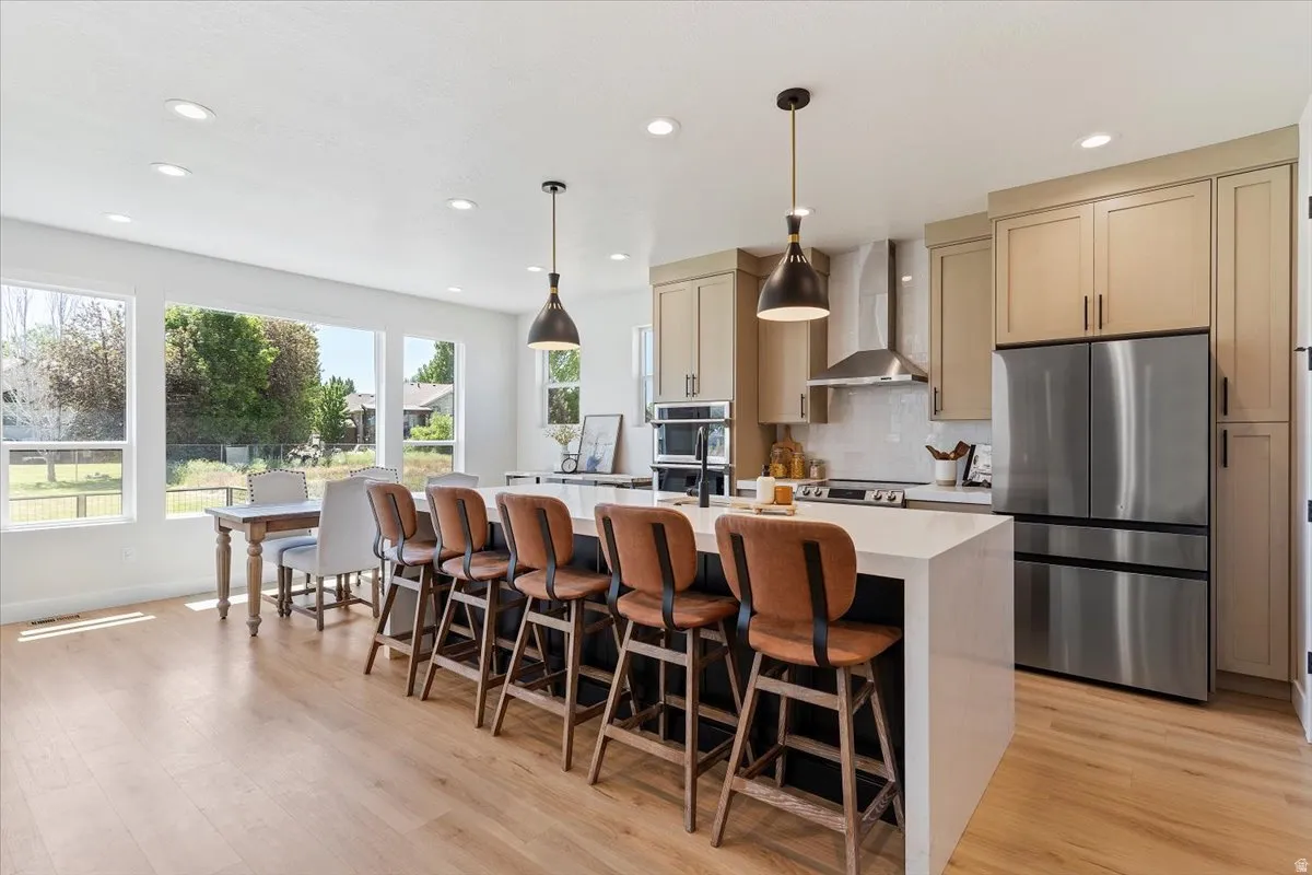 Kitchen with stainless steel appliances, a center island with sink, a breakfast bar area, light wood-style flooring, and decorative light fixtures