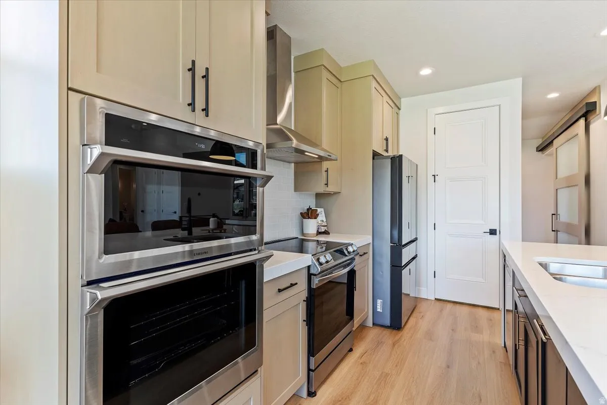 Two tone kitchen featuring stainless steel appliances, light wood-style flooring, backsplash, light stone counters, and recessed lighting