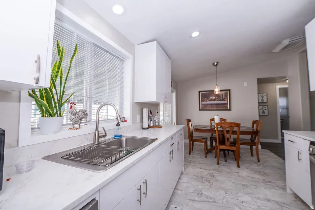 Kitchen featuring white cabinets, vaulted ceiling, hanging light fixtures, and light marble finish flooring