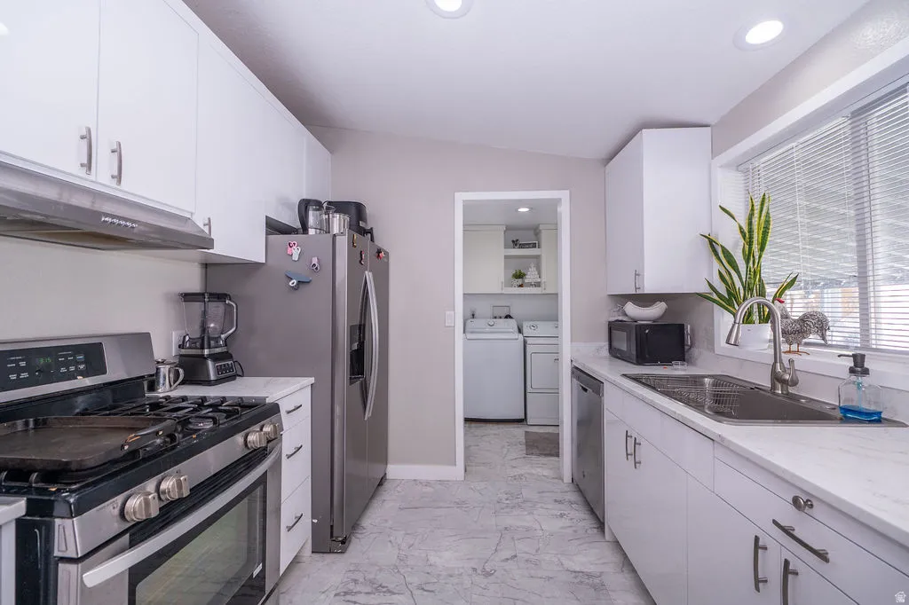 Kitchen featuring stainless steel appliances, white cabinetry, light marble finish flooring, recessed lighting, and independent washer and dryer