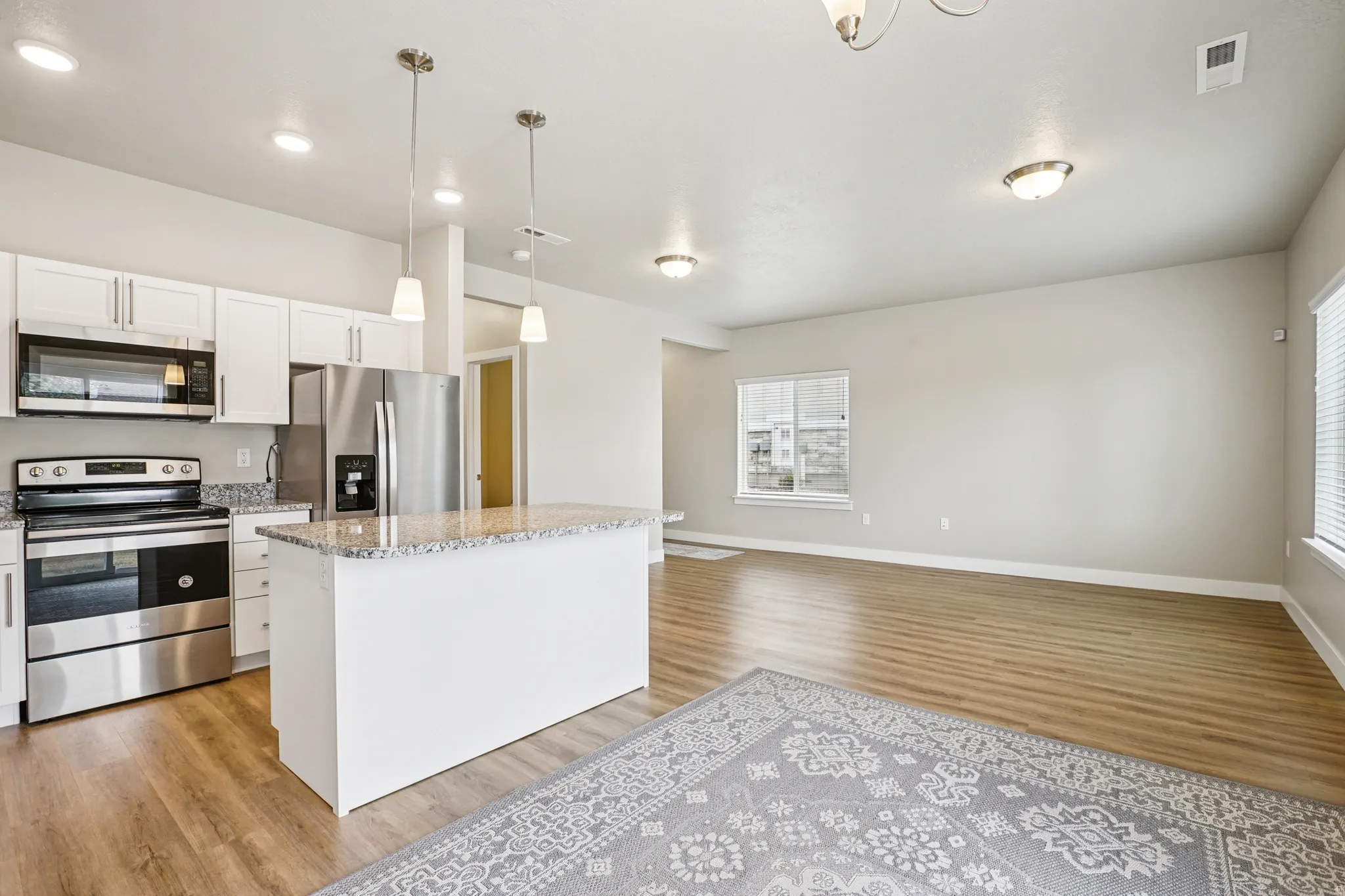 Kitchen with stainless steel appliances, white cabinets, light wood-style flooring, open floor plan, and light stone counters