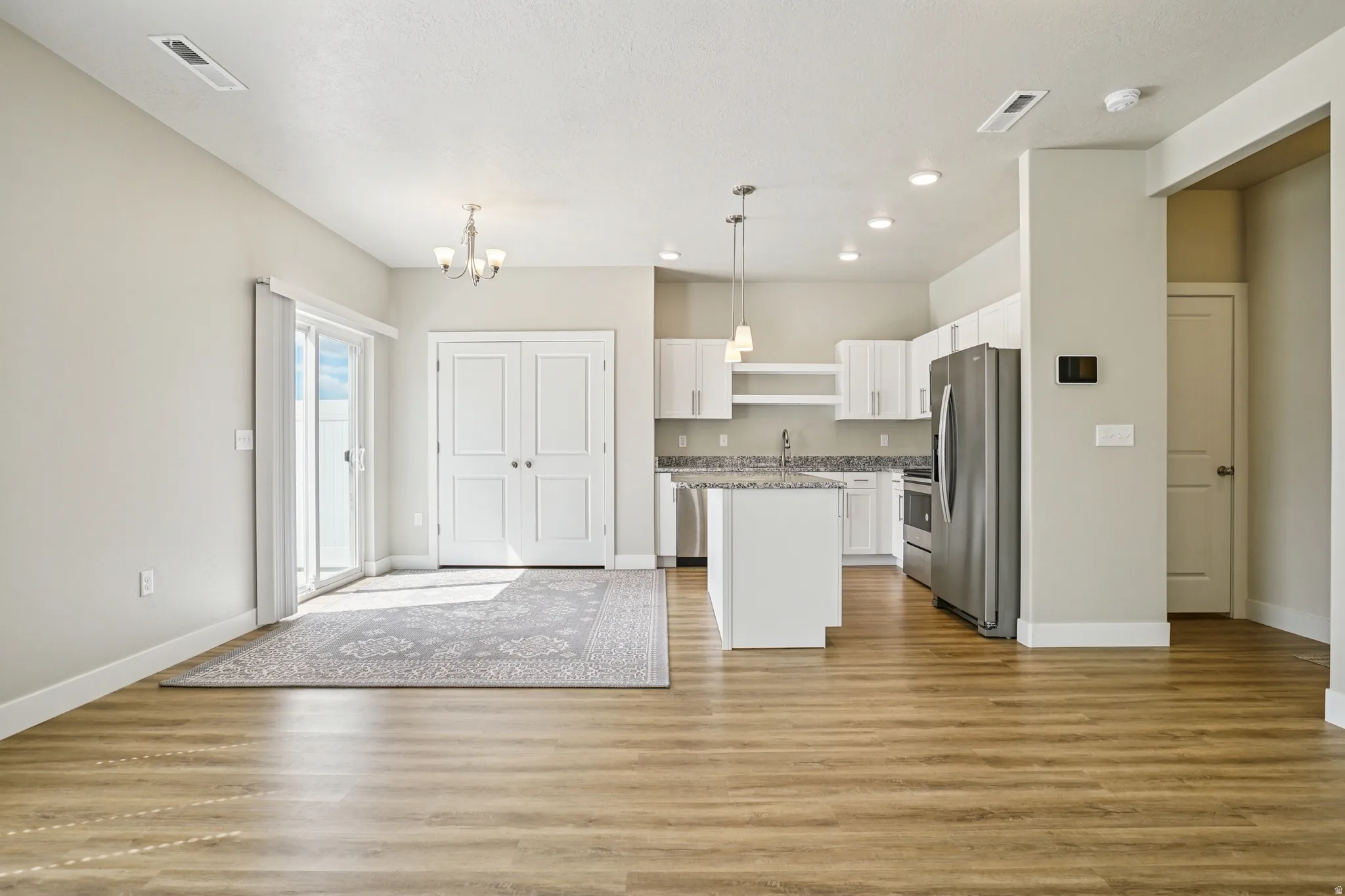 Kitchen with white cabinetry, a center island, stainless steel appliances, light wood-style flooring, and hanging lights