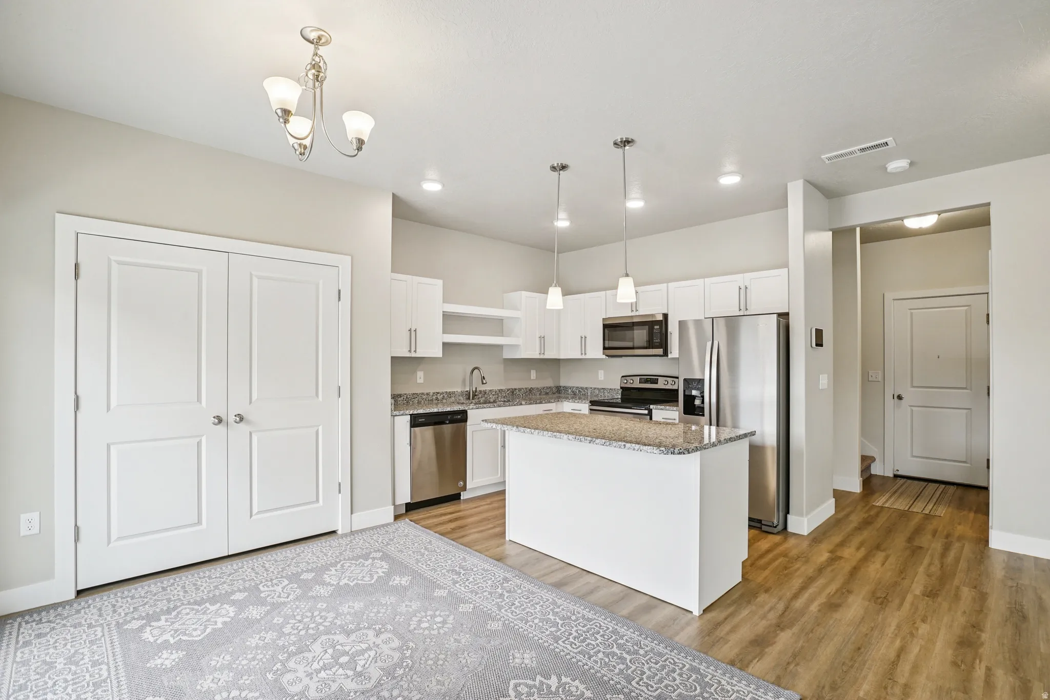 Kitchen featuring stainless steel appliances, white cabinets, light stone countertops, a kitchen island, and light wood-type flooring