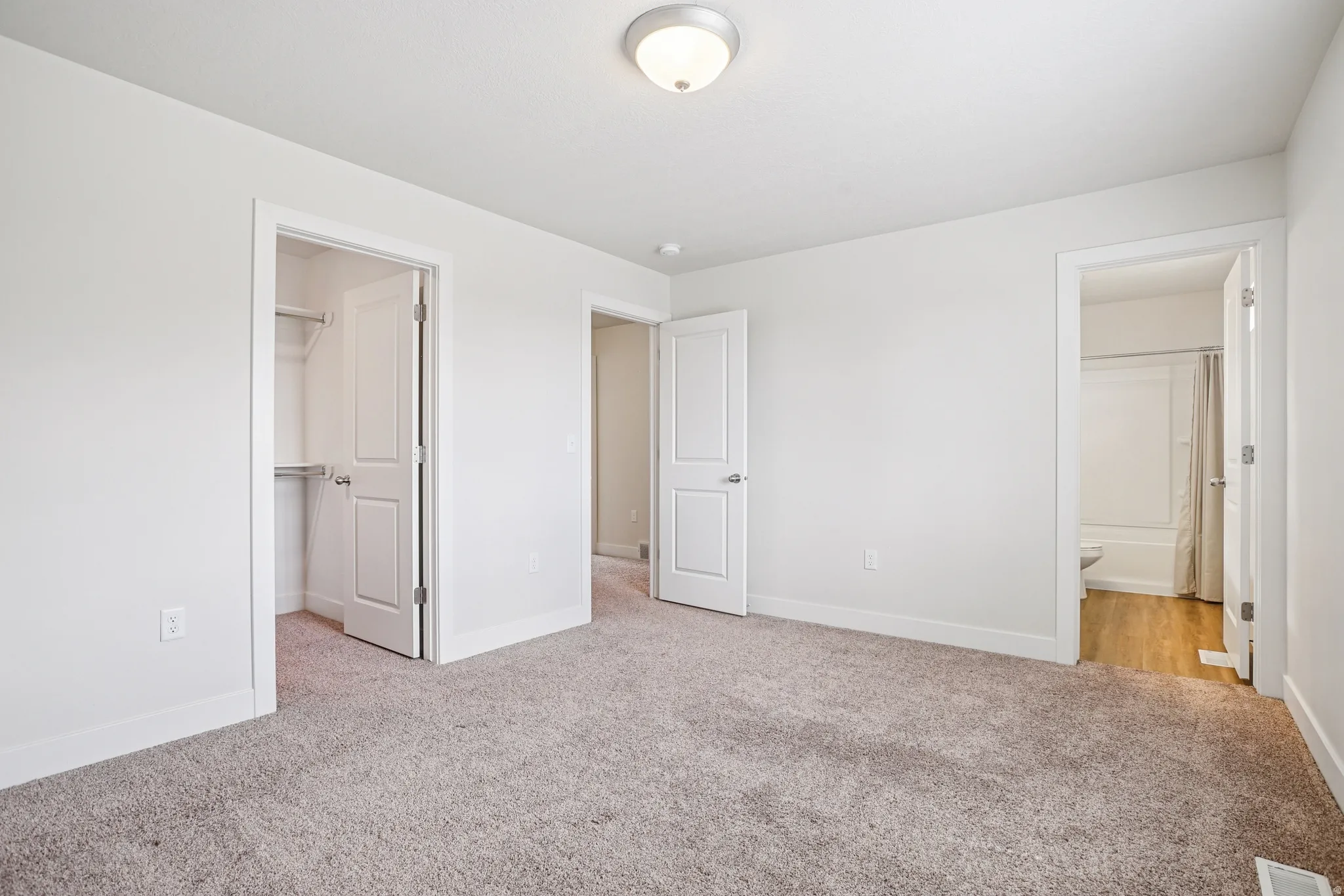 Unfurnished bedroom featuring light colored carpet, ensuite bathroom, and a spacious closet