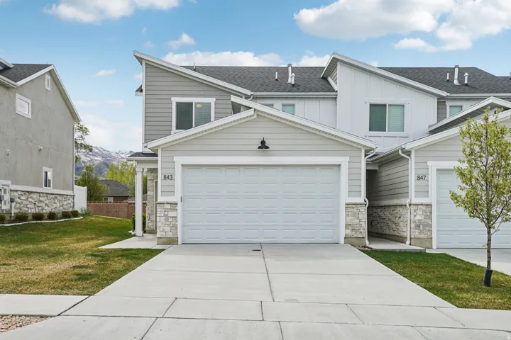 View of front of property with board and batten siding, stone siding, a front yard, and concrete driveway