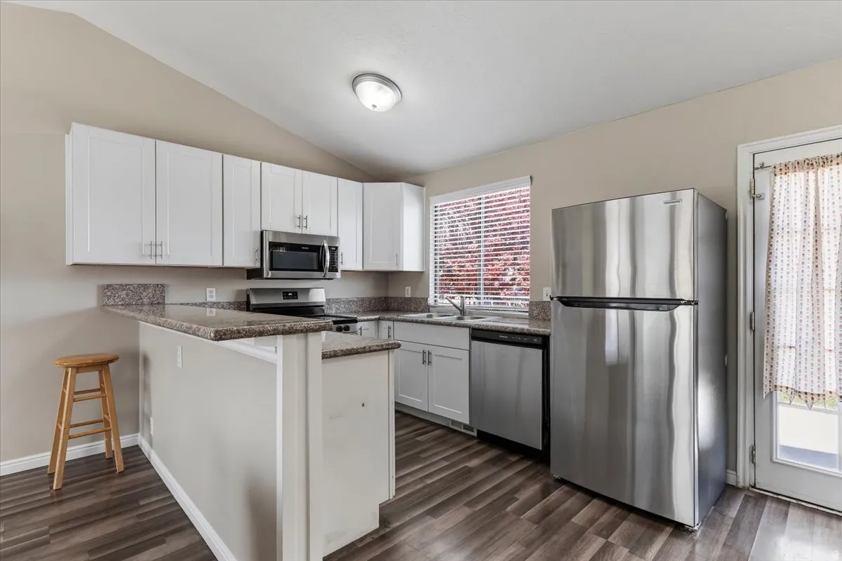 Kitchen with New stainless steel appliances, white cabinets, a peninsula, a kitchen bar, and dark stone counters