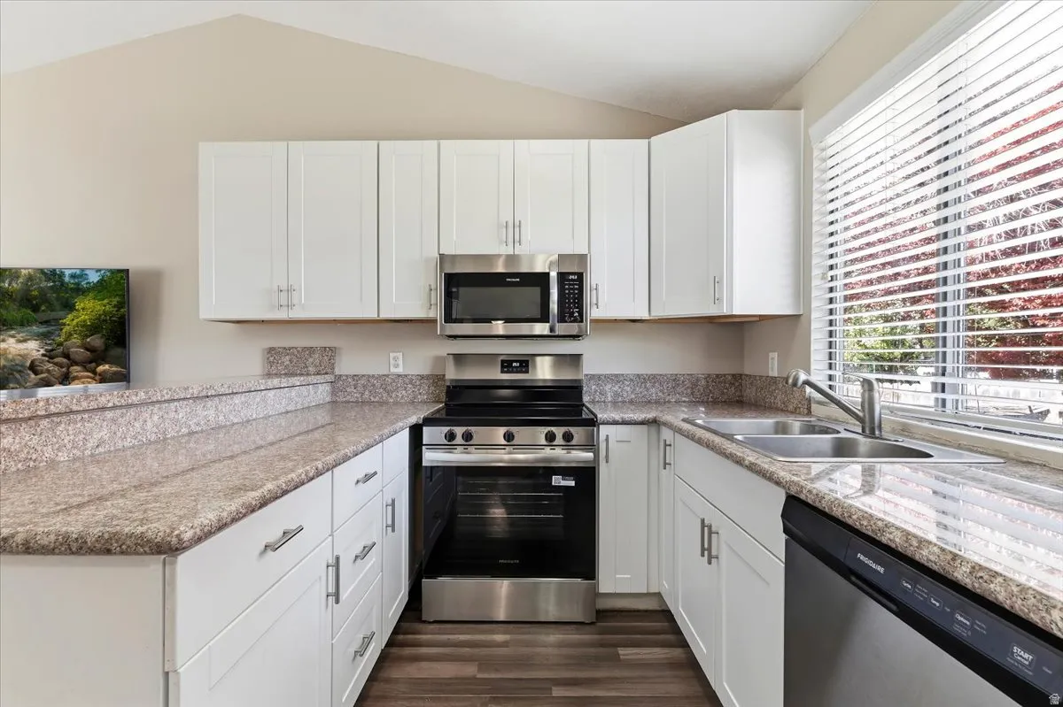Kitchen with New stainless steel appliances, white cabinetry, light stone counters, dark wood-style flooring, and lofted ceiling