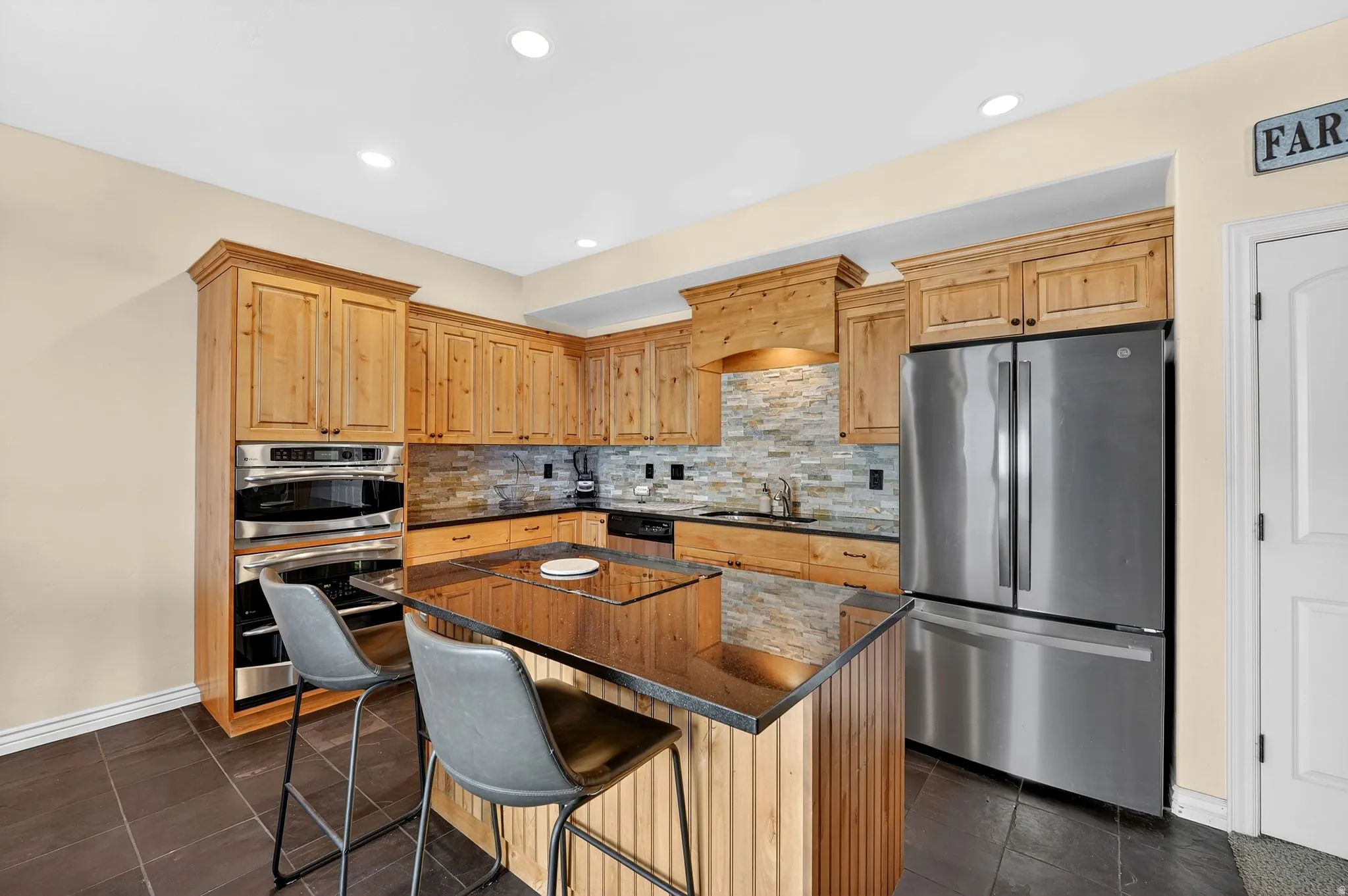 Kitchen with stainless steel appliances, a center island, a kitchen breakfast bar, dark stone counters, and backsplash