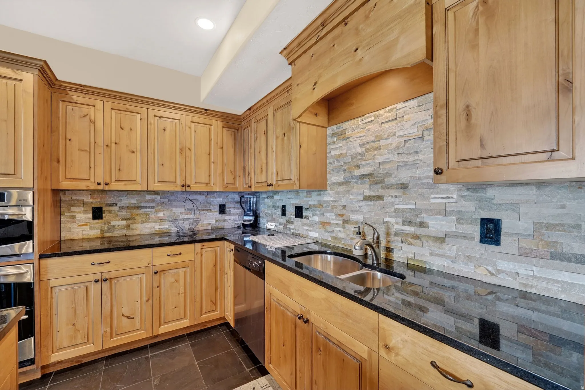 Kitchen with stainless steel appliances, light wood finish cabinets, dark stone countertops, dark tile patterned floors, and recessed lighting