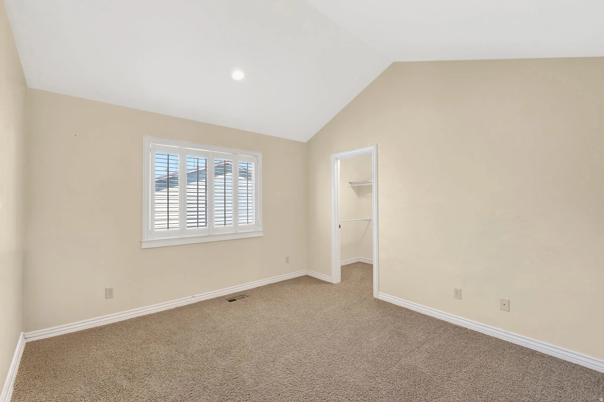 Unfurnished bedroom featuring a walk in closet, carpet flooring, and lofted ceiling