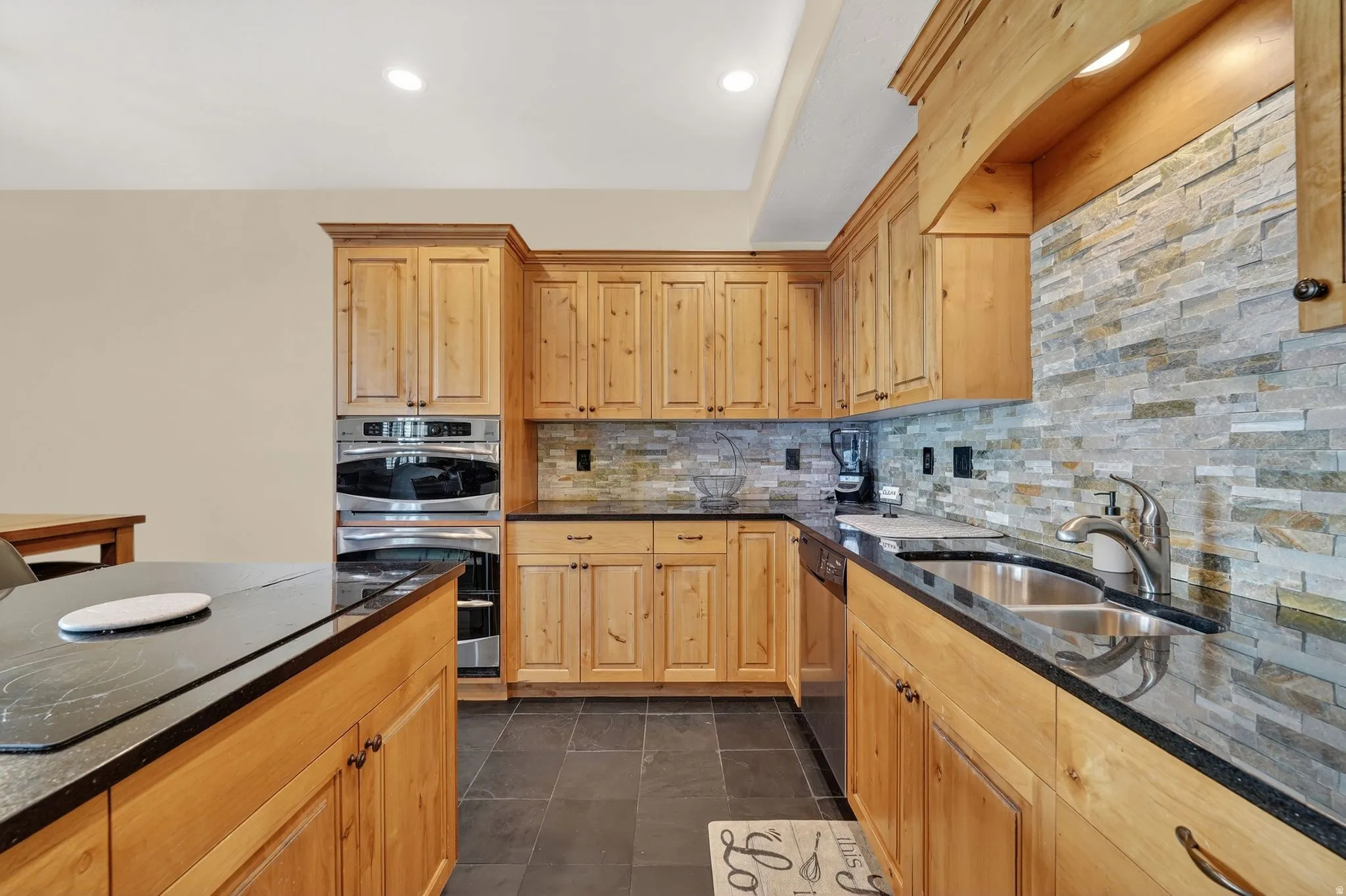 Kitchen featuring stainless steel appliances, light wood finish cabinetry, dark stone countertops, decorative backsplash, and recessed lighting