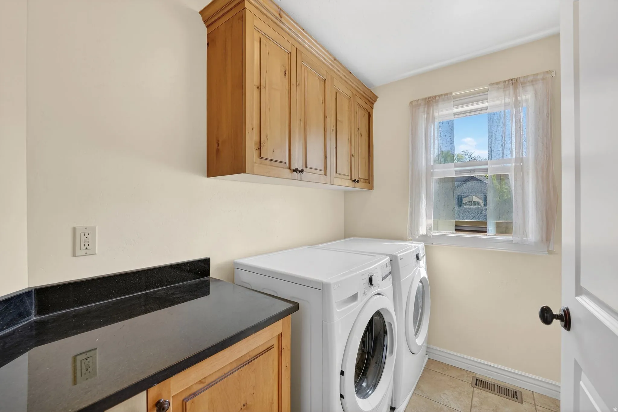 Laundry area featuring washing machine and dryer, light tile patterned flooring, and cabinet space