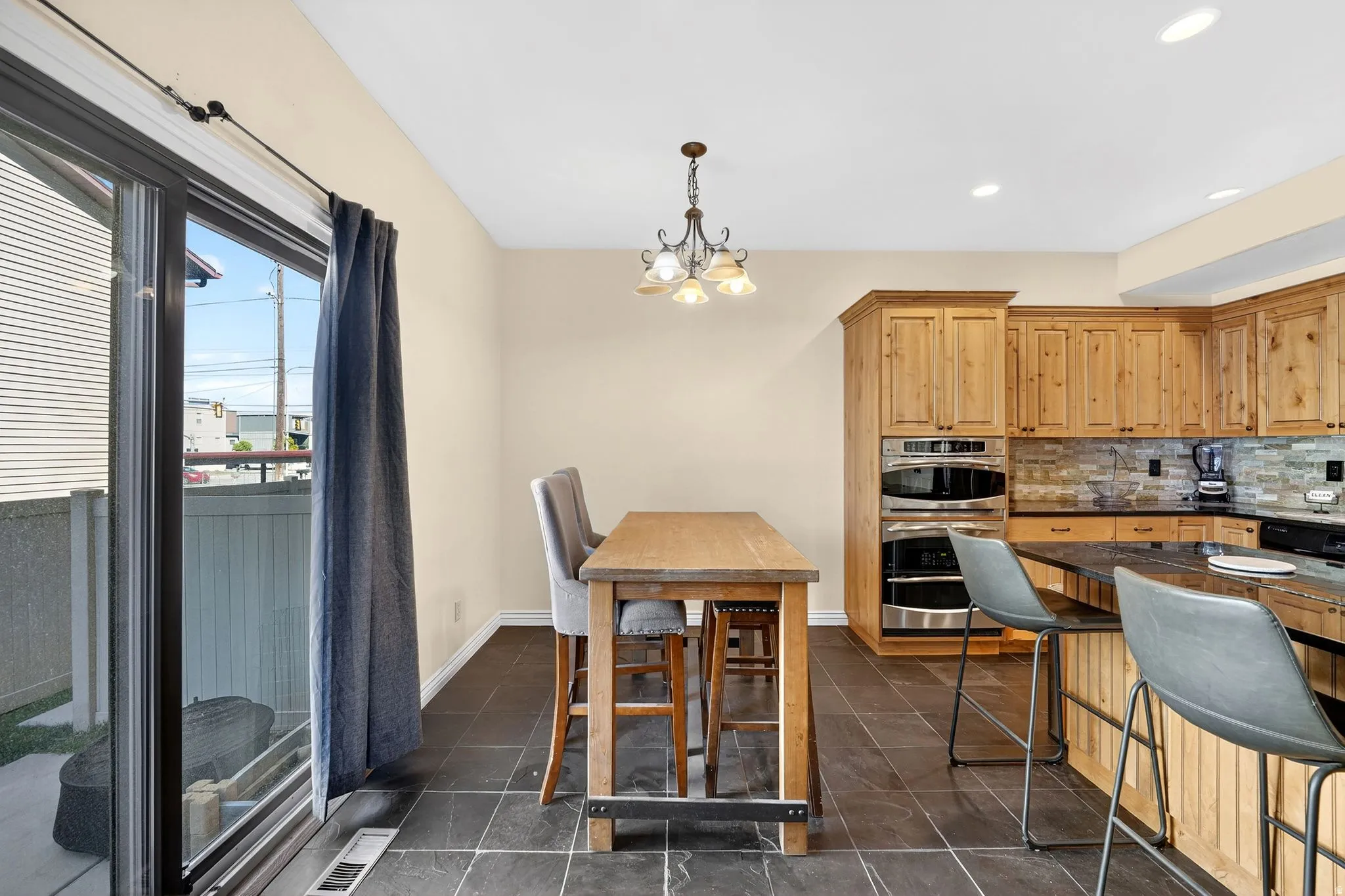 Kitchen featuring suspended lighting, double oven, decorative backsplash, dark stone counters, and a breakfast bar