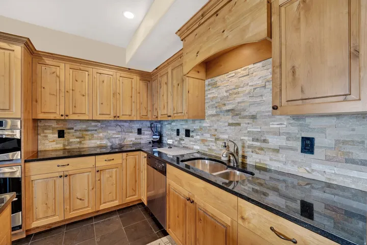 Kitchen with stainless steel appliances, light wood finish cabinets, dark stone countertops, dark tile patterned floors, and recessed lighting