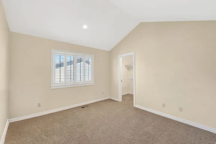 Unfurnished bedroom featuring a walk in closet, carpet flooring, and lofted ceiling