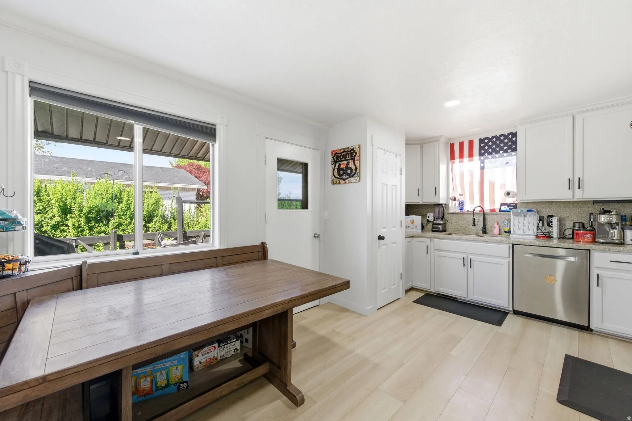 Kitchen featuring stainless steel dishwasher, white cabinetry, light wood-style flooring, and light stone countertops