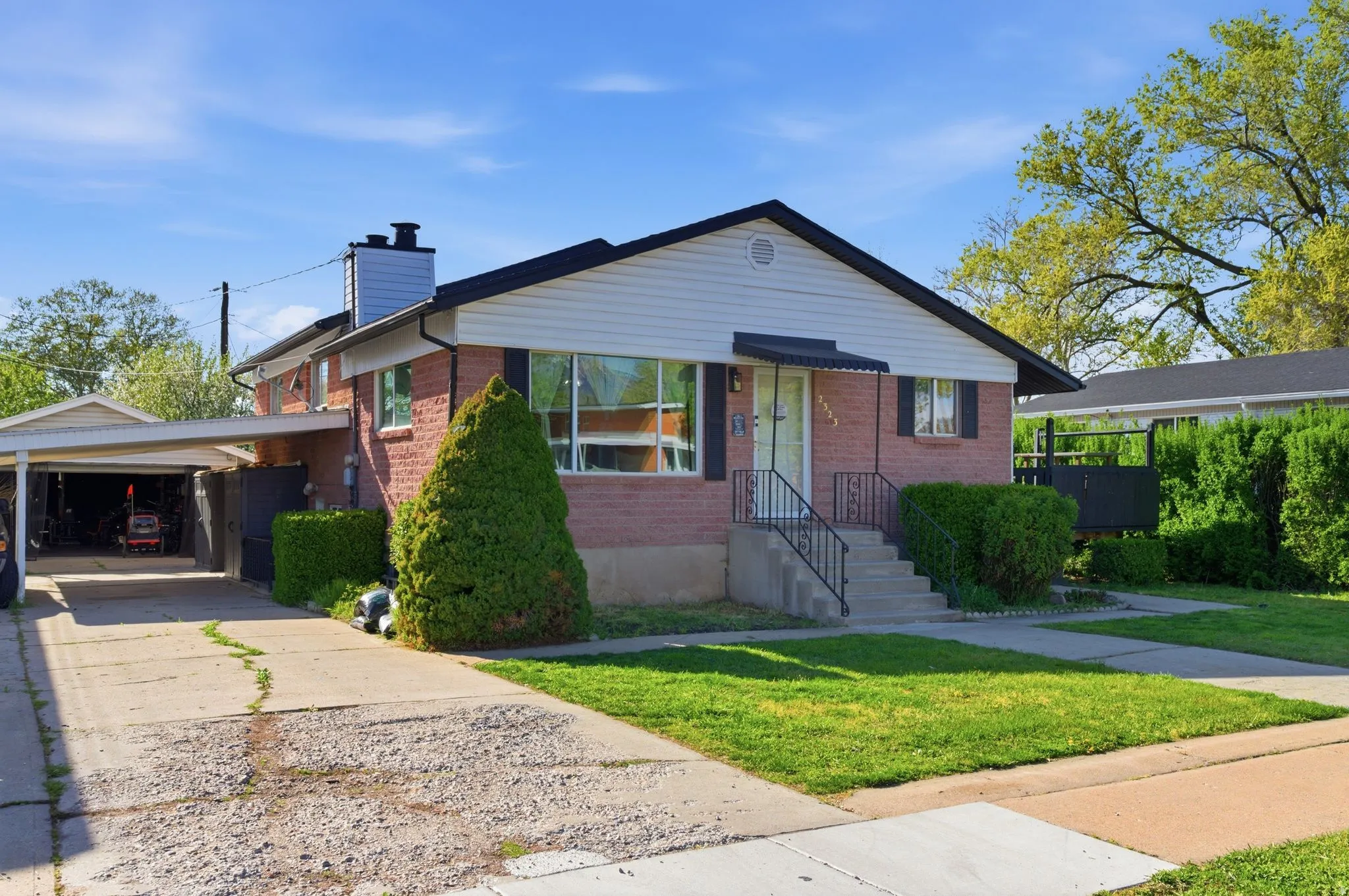 Bungalow-style home with brick siding, a chimney, a front yard, driveway, and an attached carport