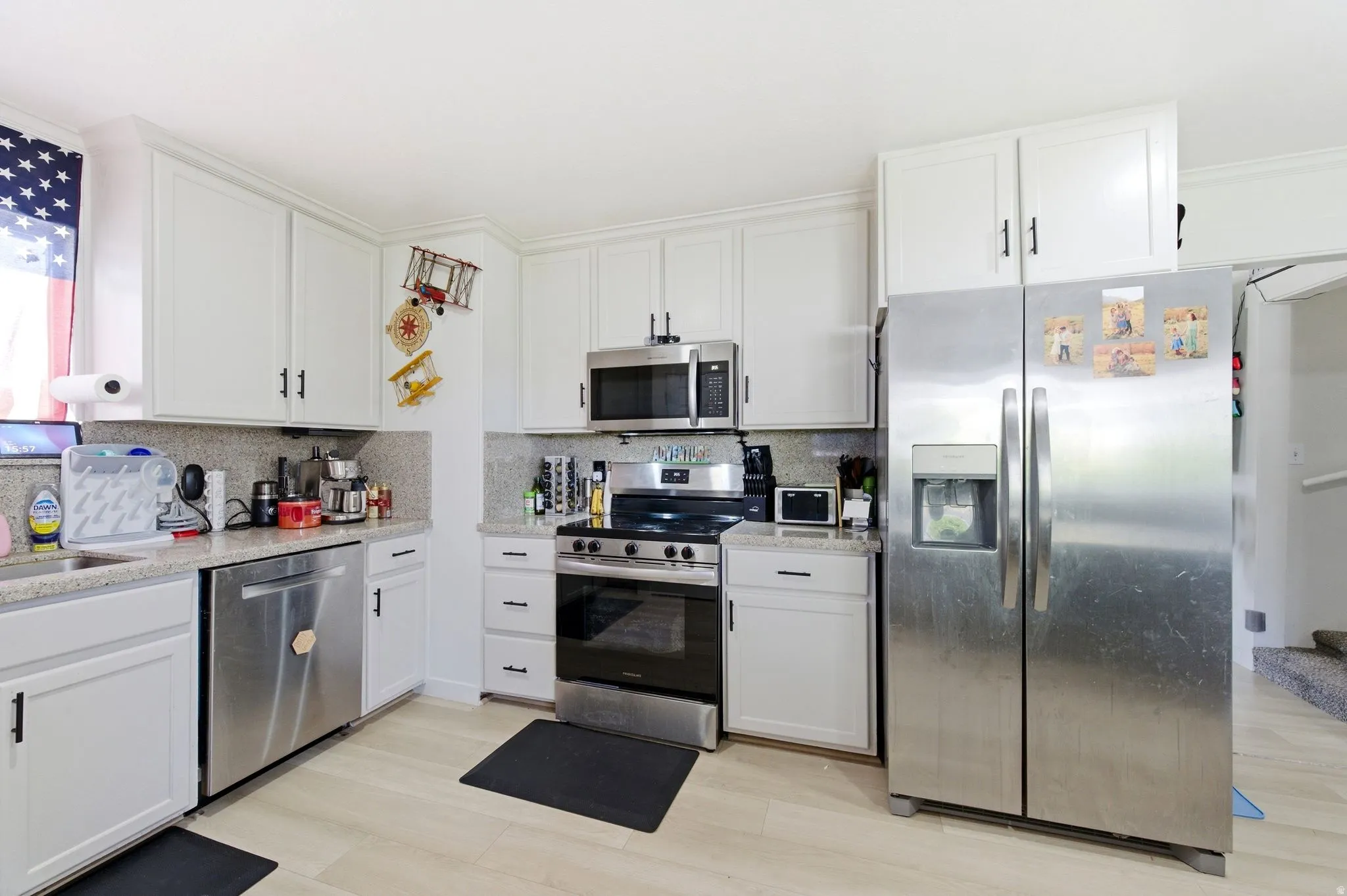 Kitchen with stainless steel appliances, white cabinetry, light stone counters, and light wood-style floors