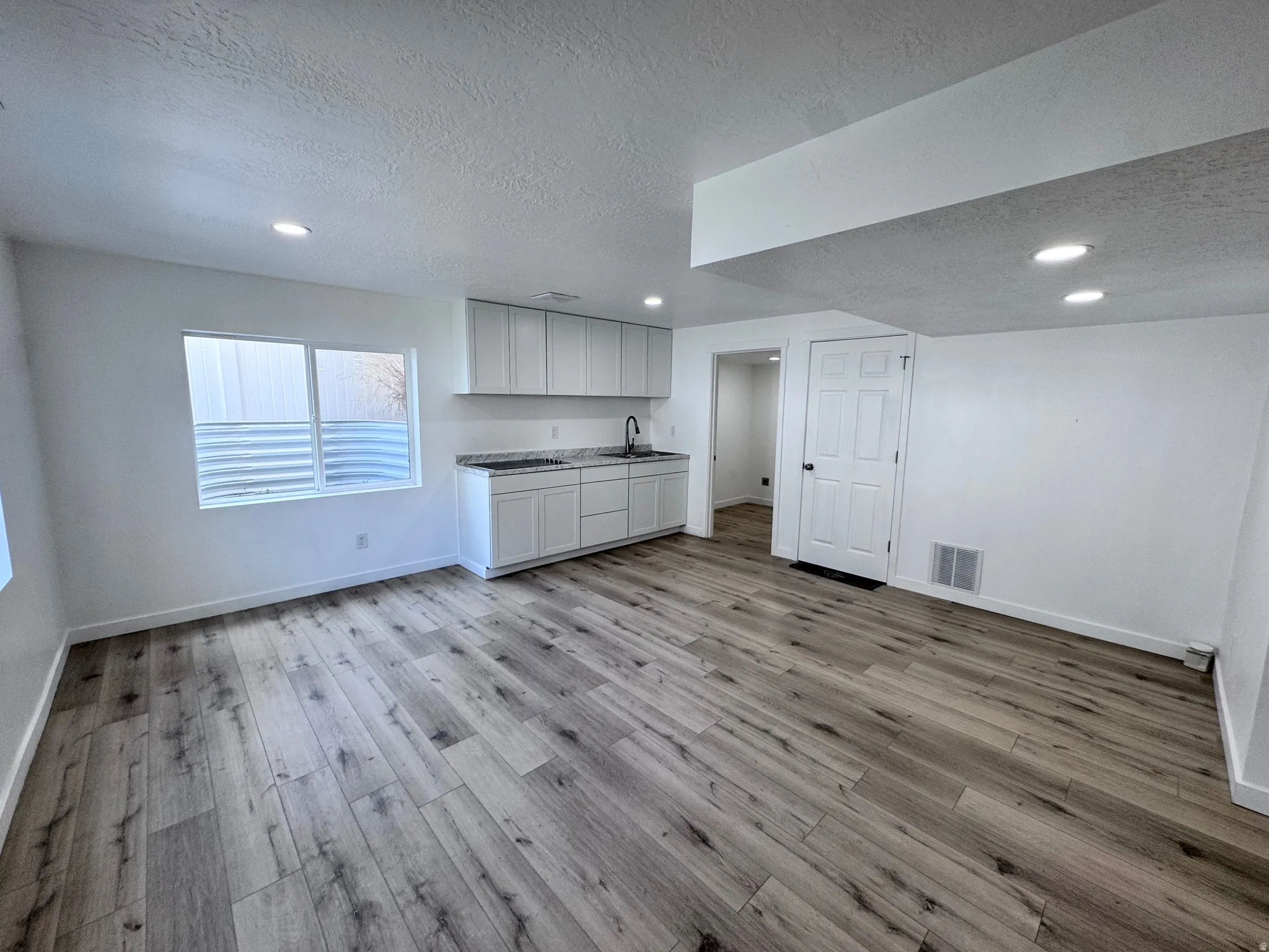 Bar featuring a textured ceiling, recessed lighting, light wood-style flooring, and white cabinetry