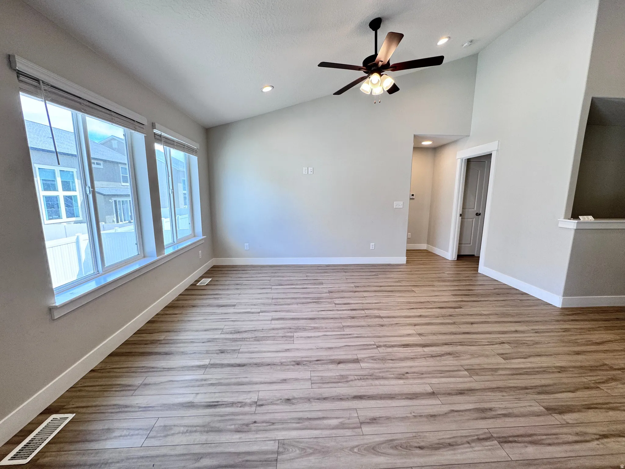 Empty room featuring ceiling fan, light wood-style floors, vaulted ceiling, and recessed lighting