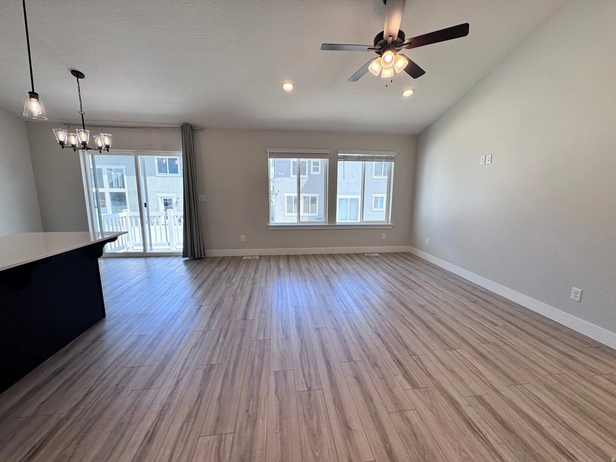 Unfurnished living room with ceiling fan, lofted ceiling, suspended lighting, and light wood-style flooring