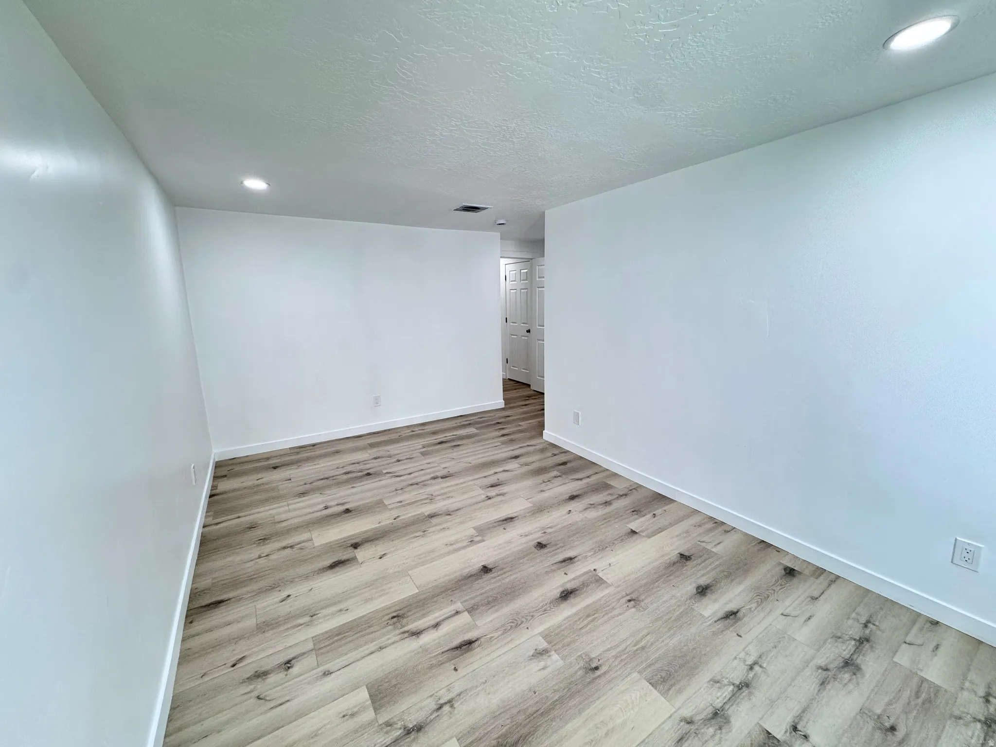 Unfurnished room featuring light wood finished floors, a textured ceiling, and recessed lighting