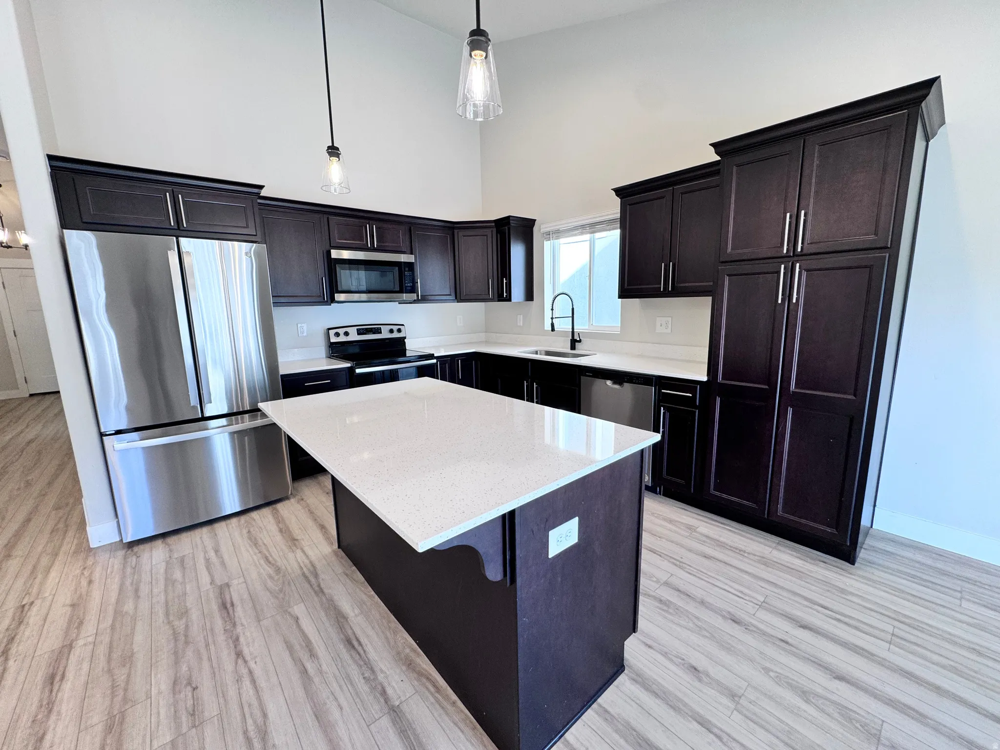 Kitchen featuring a high ceiling, stainless steel appliances, a kitchen island, light wood-style floors, and light stone counters