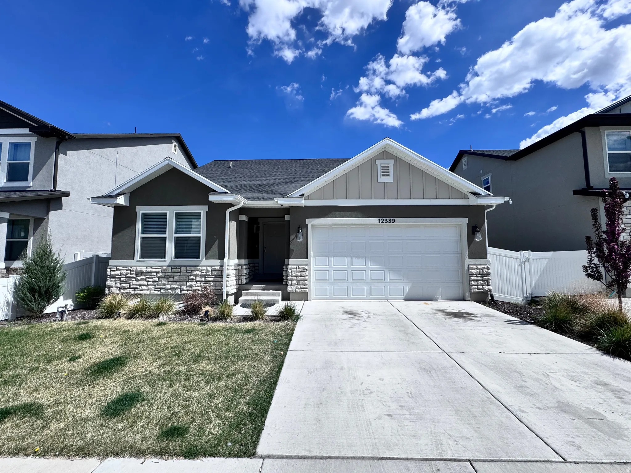 View of front of house with a garage, concrete driveway, board and batten siding, stone siding, and stucco siding